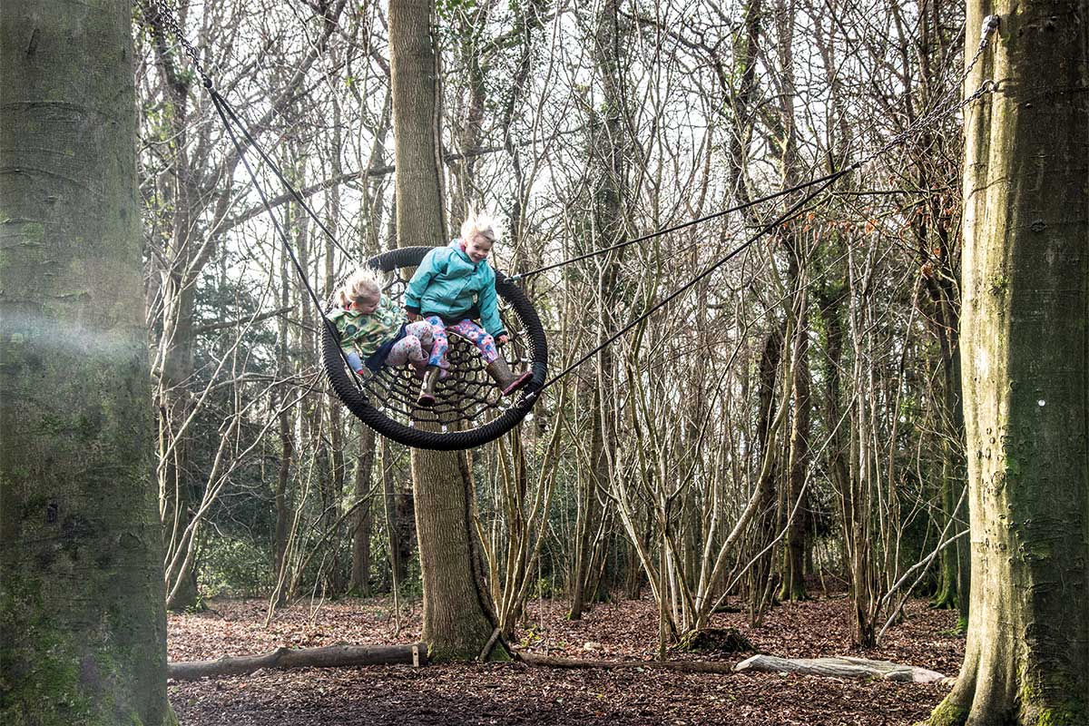 Colour photo of two children swinging on basket swing between two trees in Leigh Woods playground