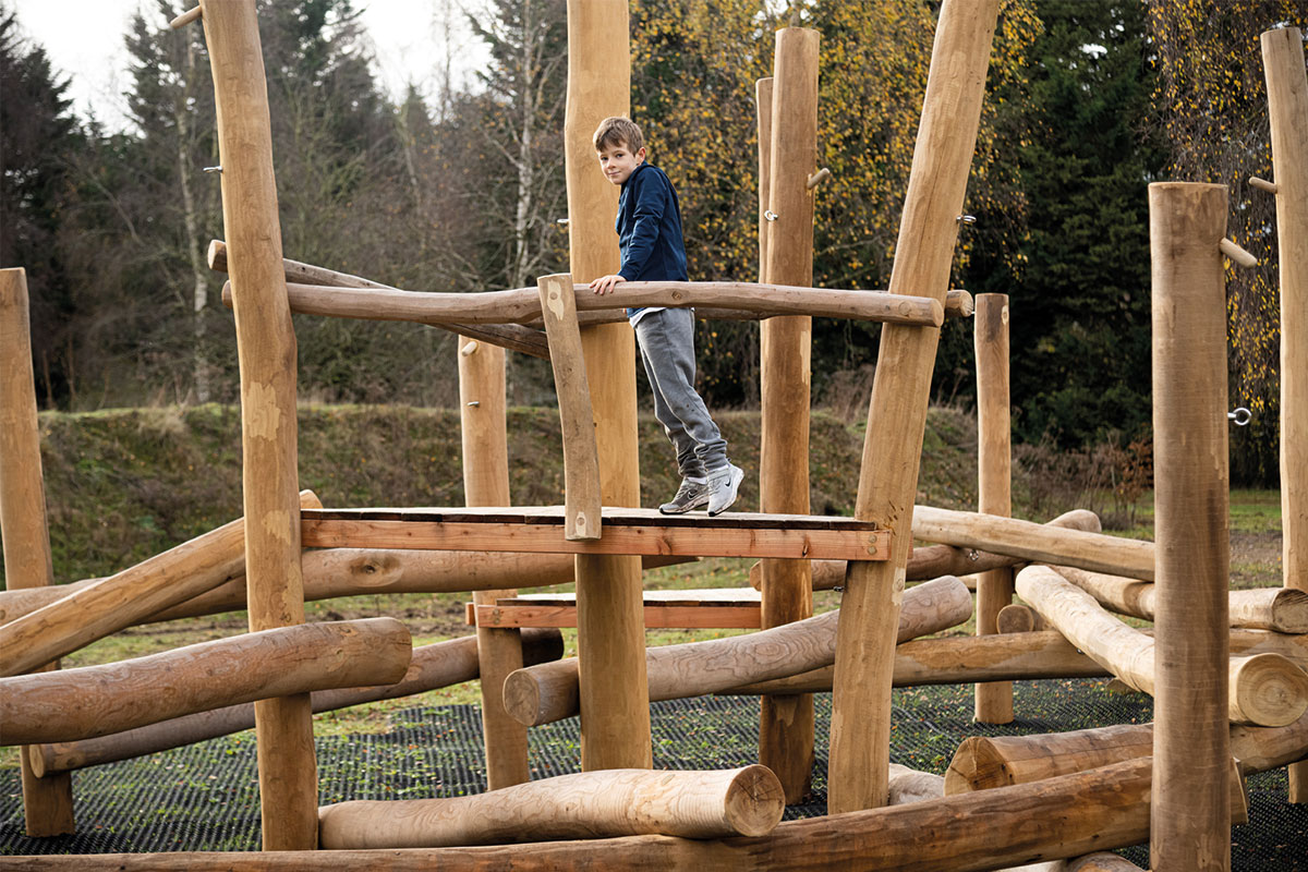 Colour photo of child standing on wooden balance log at Bainland Lodge Retreats adventure playground