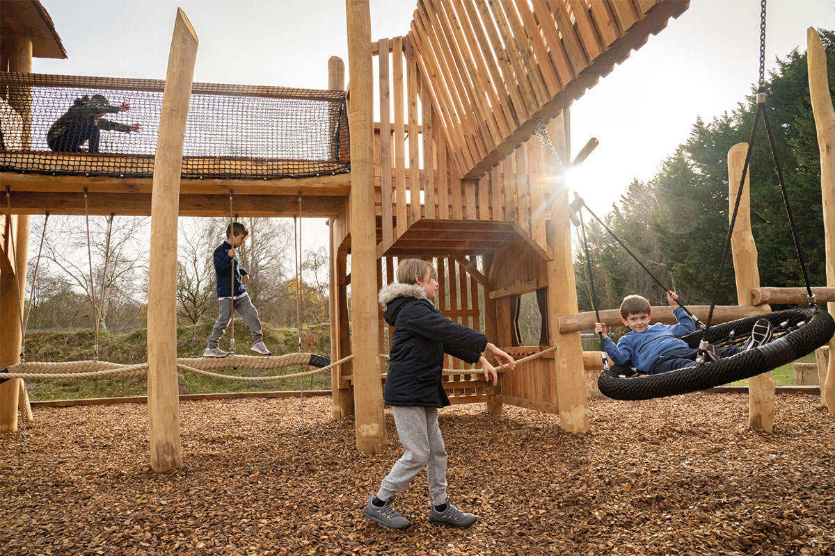 Colour photo of children playing on basket wing attached to natural wooden tower and net bridge at Bainland Lodge Retreat adventure playground
