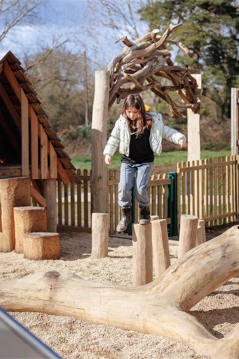 Colour photo of child balancing on wooden log hops in playground