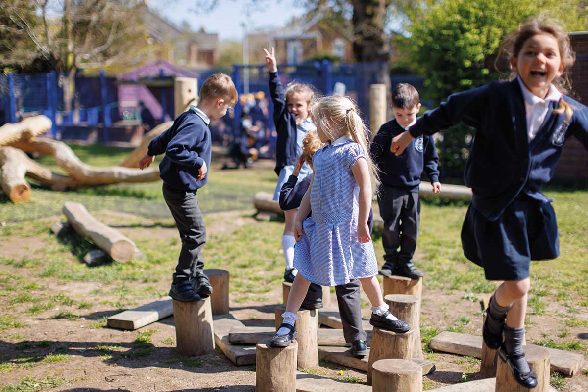Colour photo of young children in school uniform balancing on wooden log hops in school playground