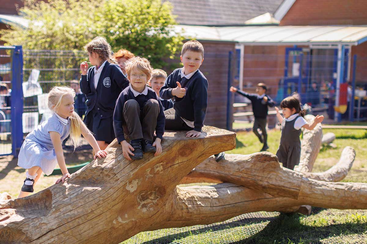 Colour photo of young children climbing and playing on natural wooden climbing log in school playground