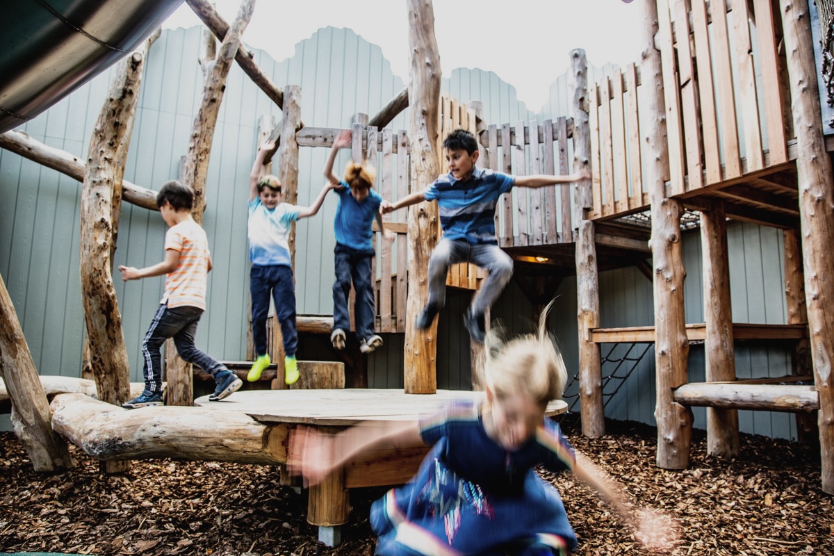 Colour photo of children balancing on log beams on wooden adventure playground