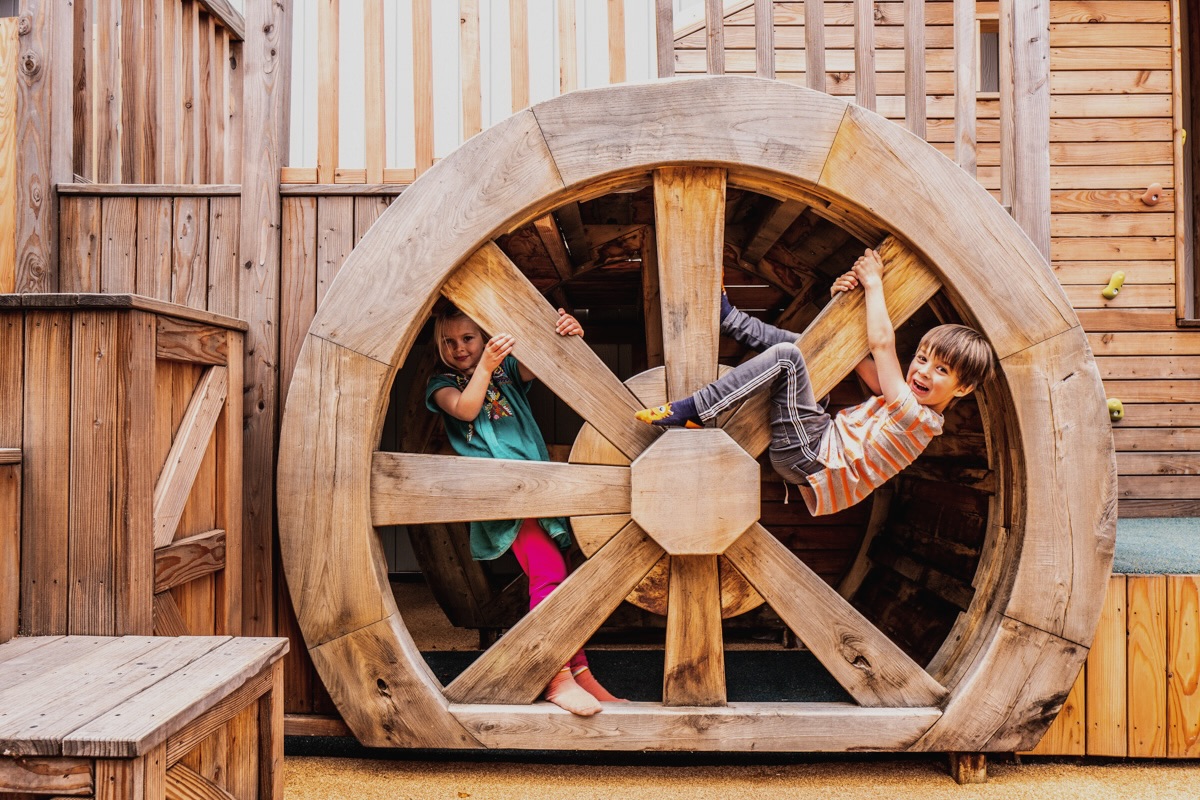 Colour photo of children playing on wooden wheel at Bicester Village adventure playground
