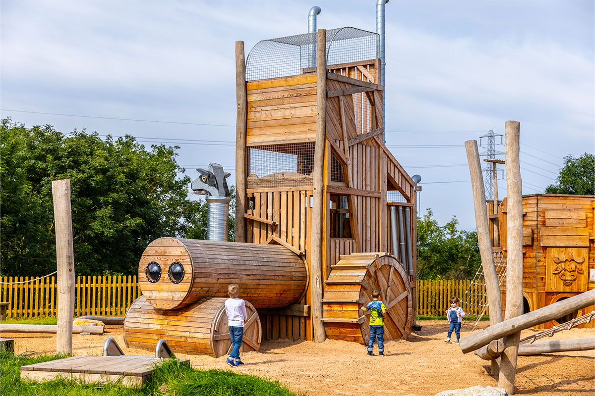 Colour photo of large wooden tractor adventure playground structure, with children playing around it