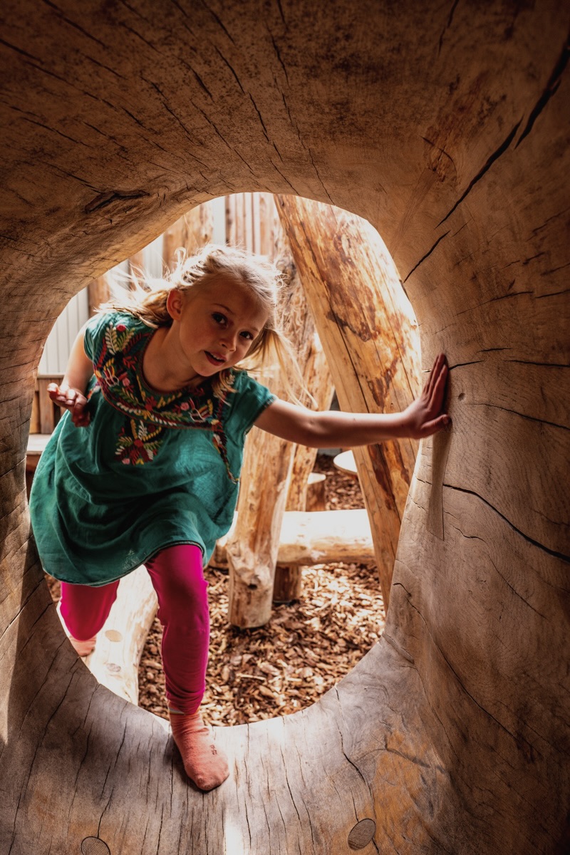 Colour photo of young girl climbing inside wooden hollow log