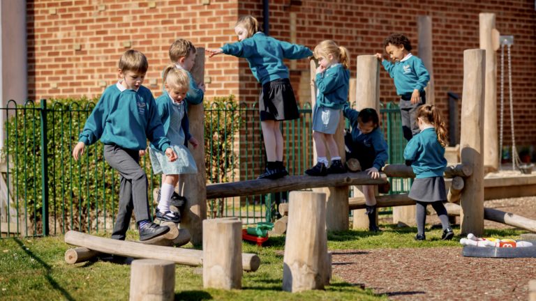 Colour photo of children playing on wooden climbing blocks at Stanley Green Infant Academy