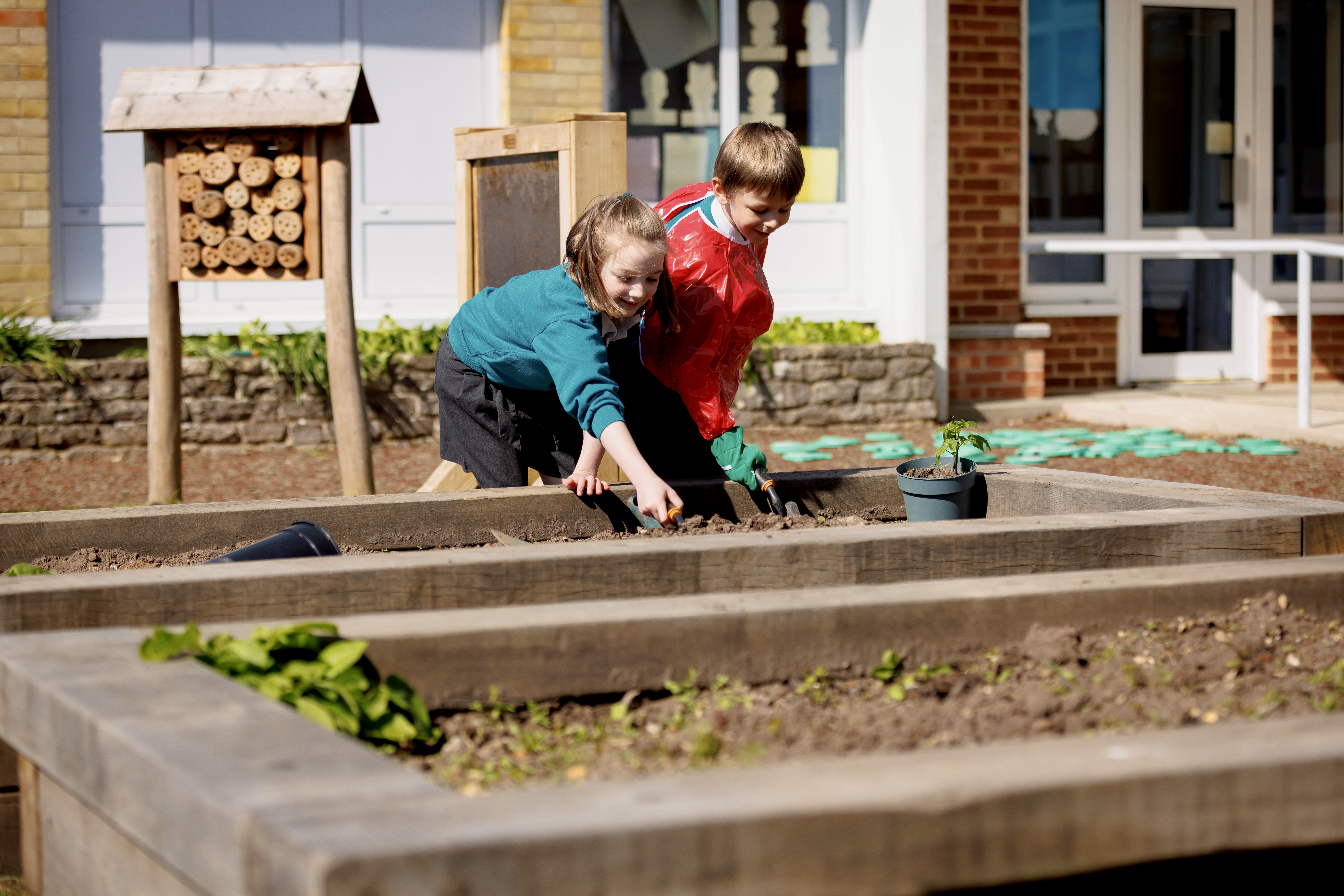 Colour photo of two children planting seeds in wooden planter at Stanley Green school playground