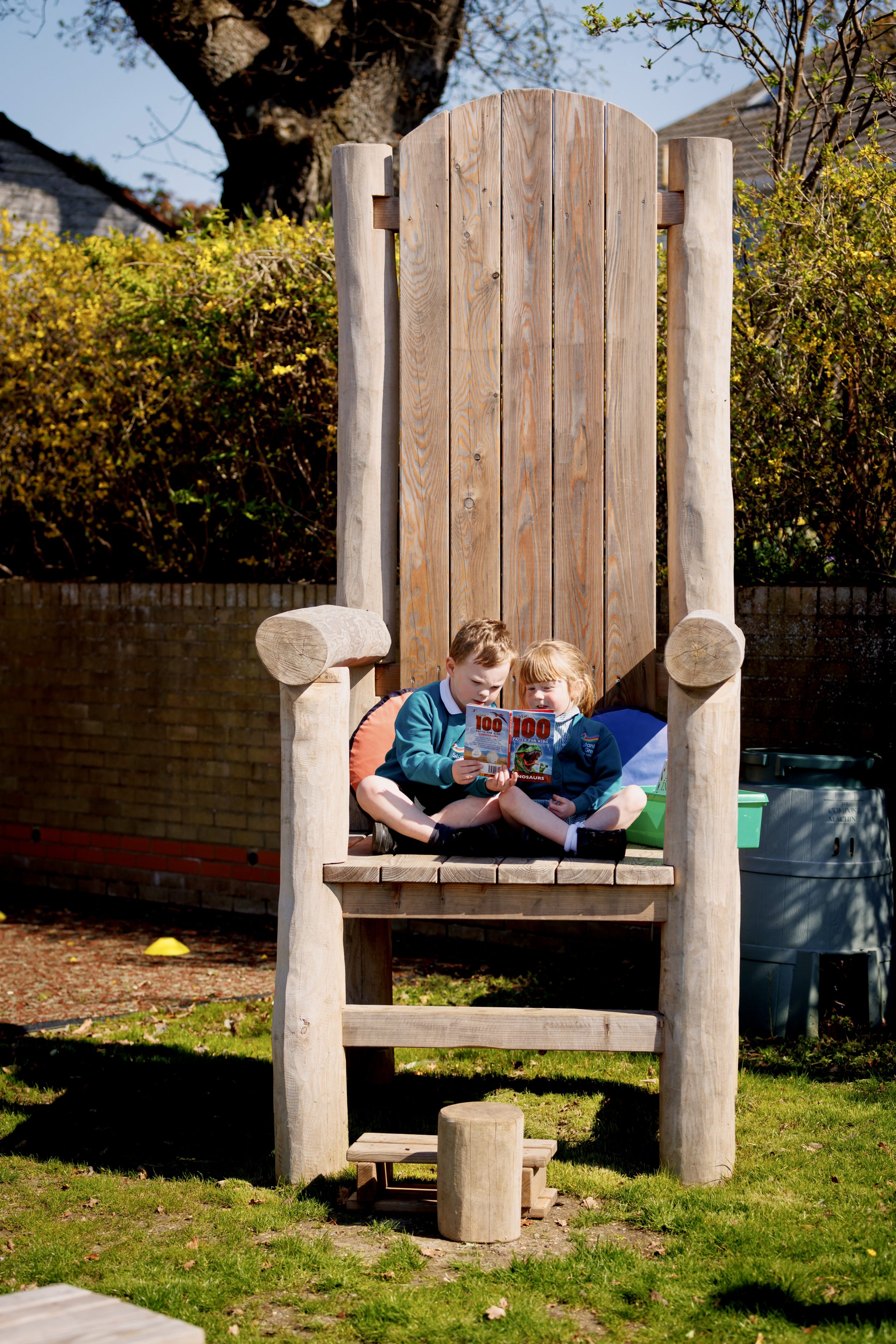 Colour photo of two children sitting on giant wooden chair reading books at Stanley Green school playground