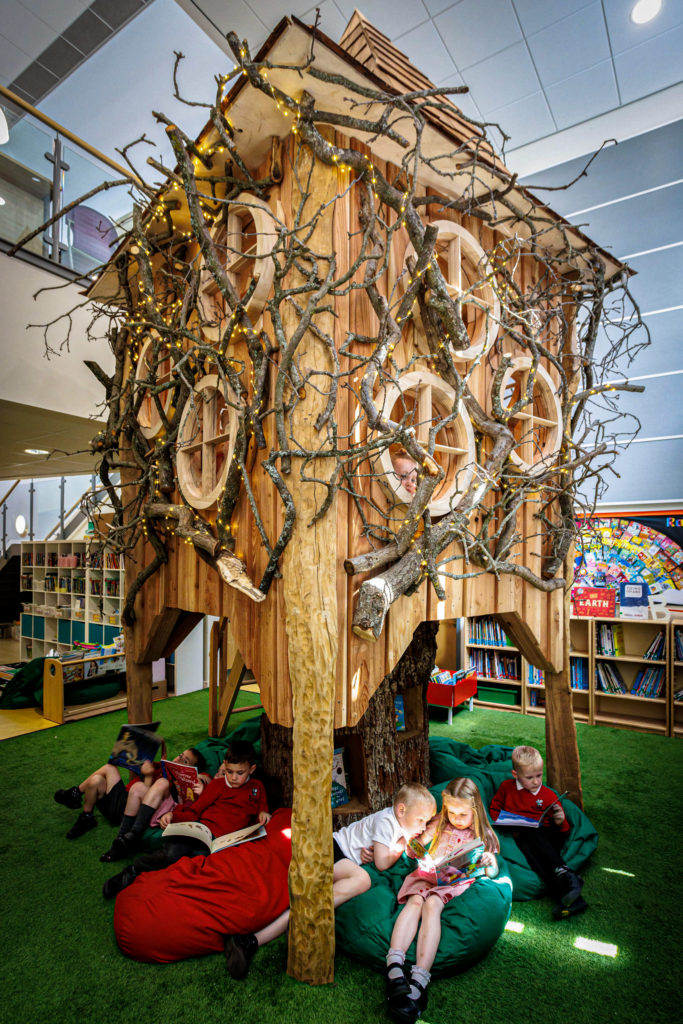 A wooden indoor play tower with bean bags underneath and children reading the books