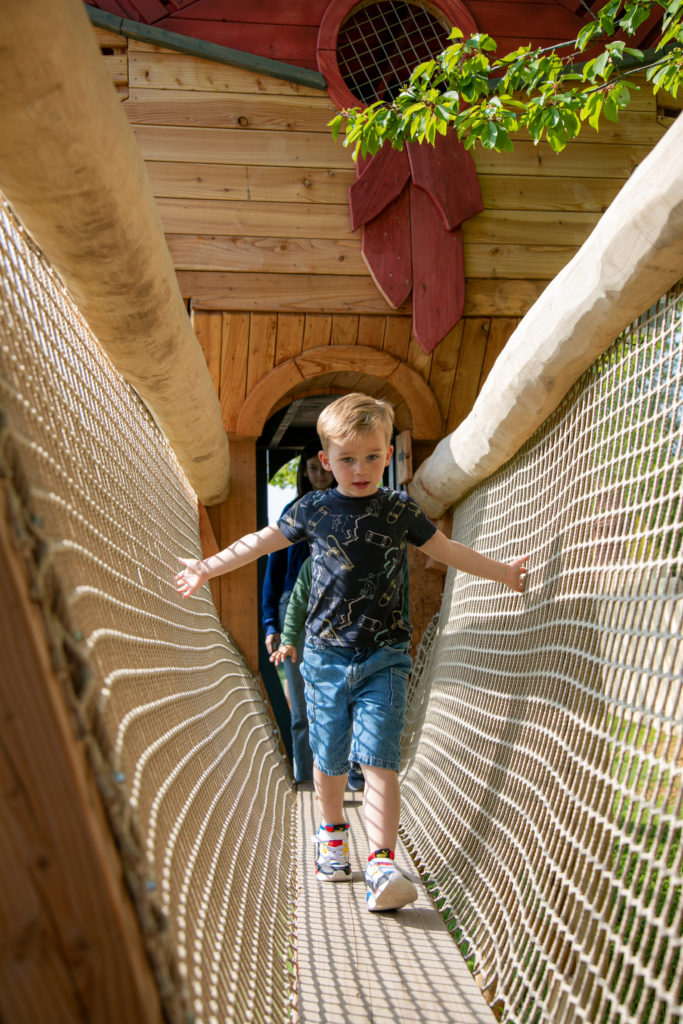A small boy risking to walk on a wooden playground structure holding onto the net