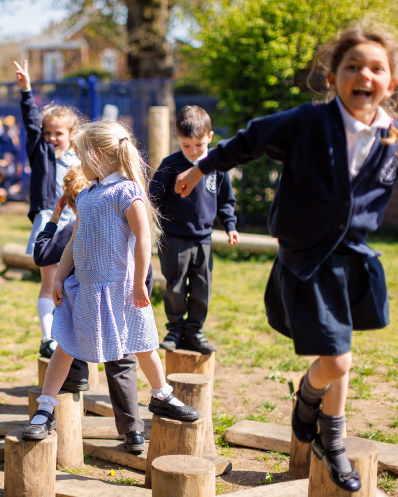 Children in school uniforms playing on hop log stumps play equipment in a sunny playground