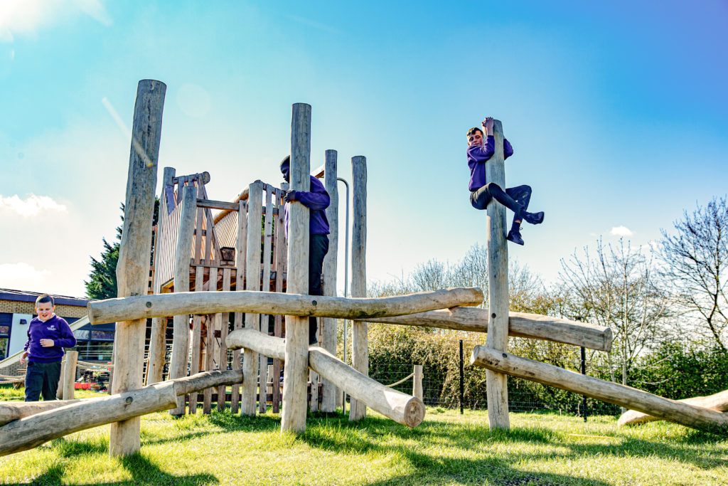 Three children interacting with a robust wooden playground timber tangle structure.
