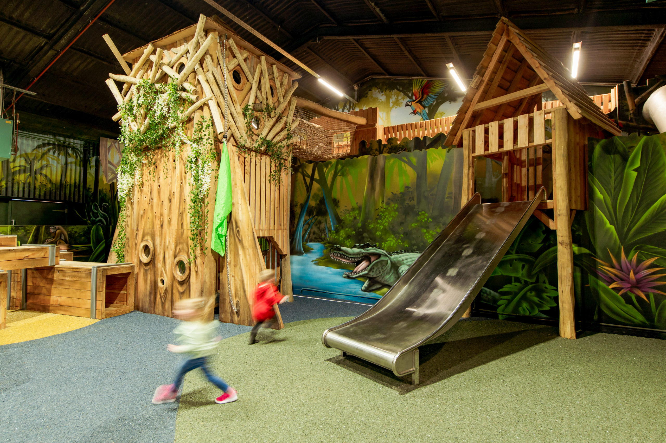A vibrant and creatively designed indoor jungle-themed playground with children in motion.