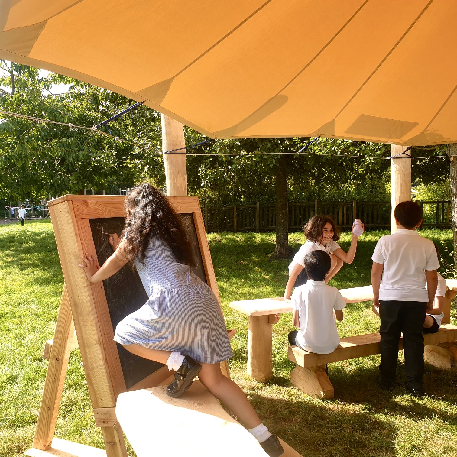 a girl drawing on a board under a canopy of an outdoor classroom.